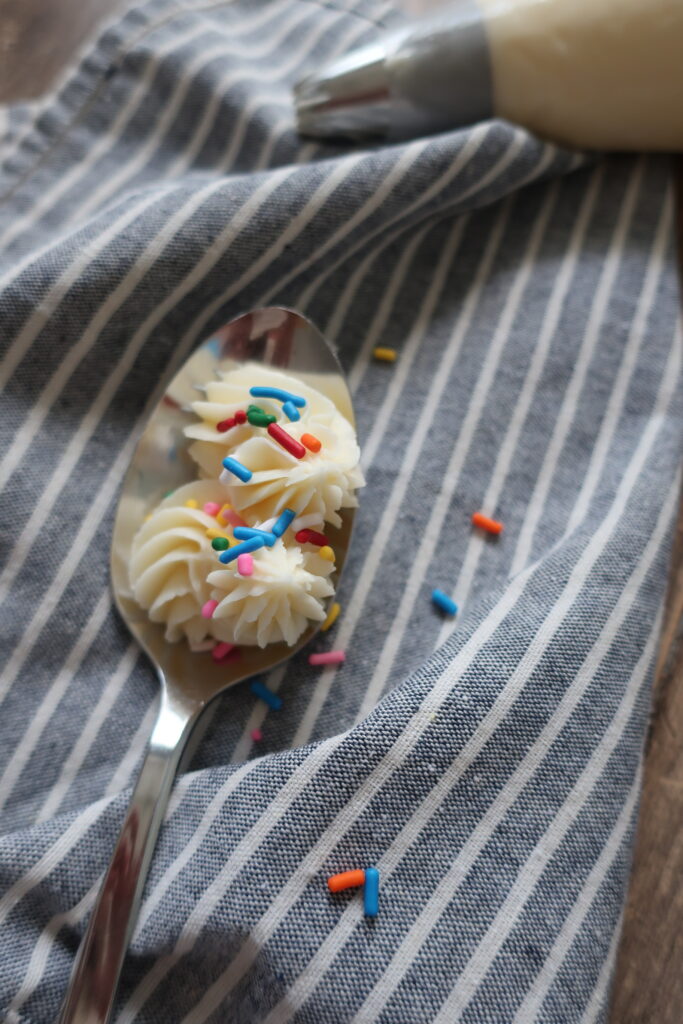 vanilla buttercream frosting topped with sprinkles on spoon sitting on blue striped napkin