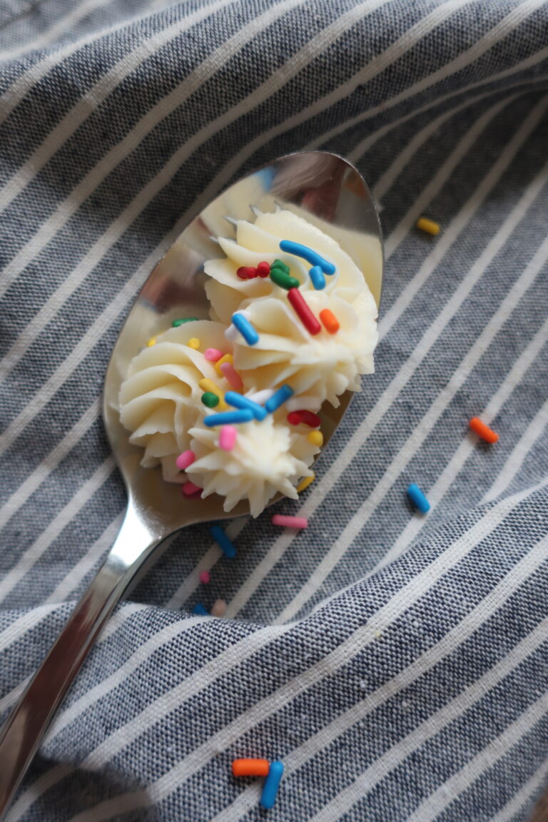 vanilla buttercream frosting topped with sprinkles on spoon sitting on blue striped napkin