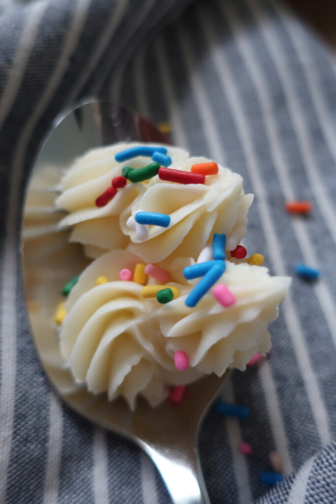 vanilla buttercream frosting topped with sprinkles on spoon sitting on blue striped napkin