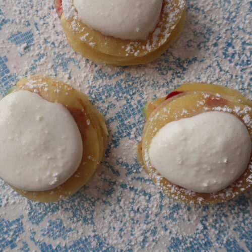 mini crepes formed into stacks layered with homemade raspberry sauce, homemade lemon curd, and homemade whipped cream, and dusted with powdered sugar