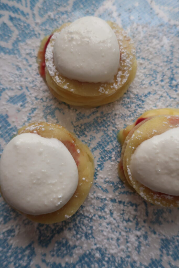 mini crepes formed into stacks layered with homemade raspberry sauce, homemade lemon curd, and homemade whipped cream, and dusted with powdered sugar