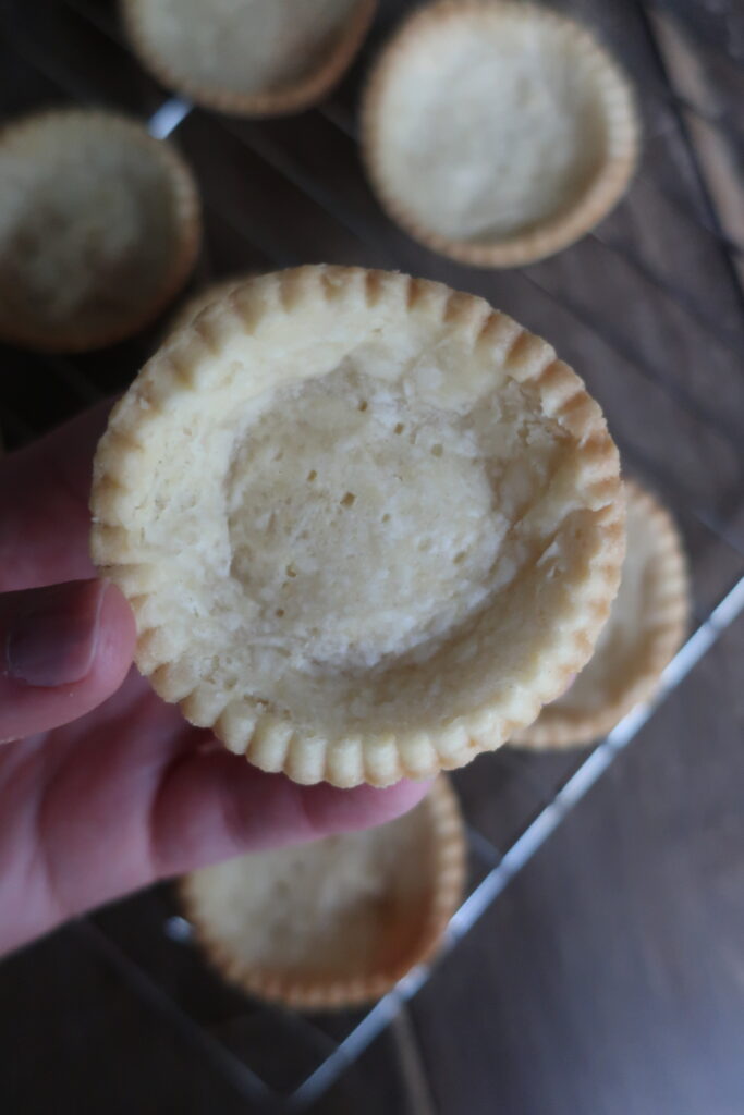 pastry crust for mini fruit tarts with pastry cream, raspberry sauce, and fresh fruit (blueberries and orange); mini pie crust on wire rack