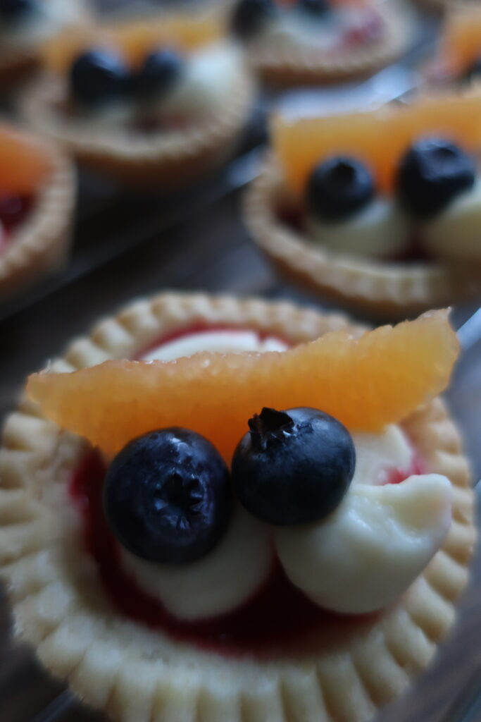 pastry crust for mini fruit tarts with pastry cream, raspberry sauce, and fresh fruit (blueberries and orange); mini pie crust on wire rack