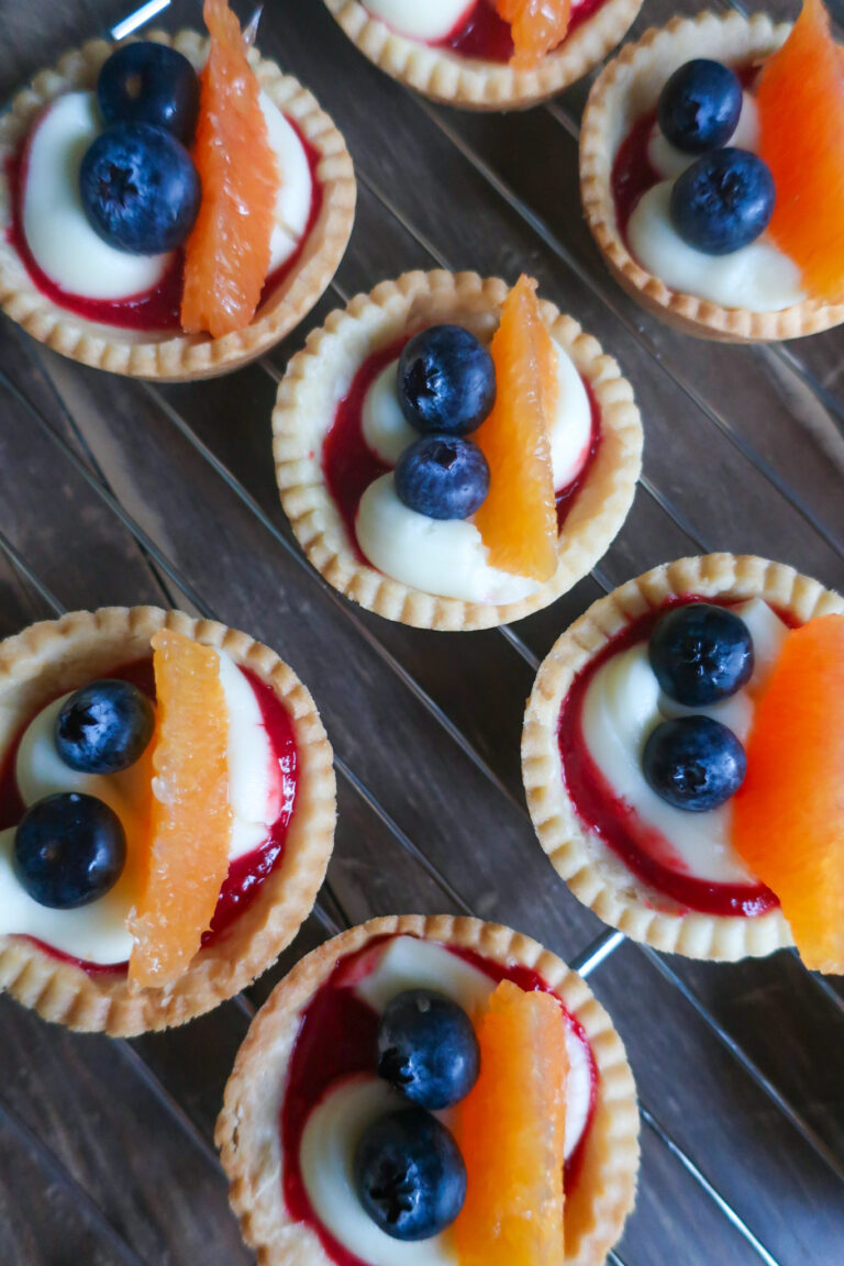 pastry crust for mini fruit tarts with pastry cream, raspberry sauce, and fresh fruit (blueberries and orange); mini pie crust on wire rack