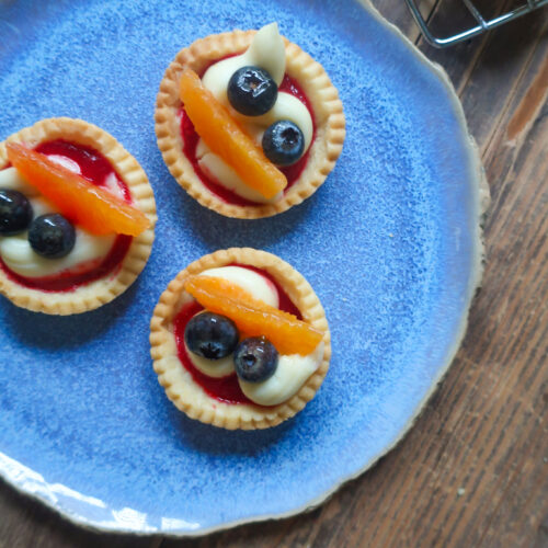 pastry crust for mini fruit tarts with pastry cream, raspberry sauce, and fresh fruit (blueberries and orange); mini pie crust on wire rack