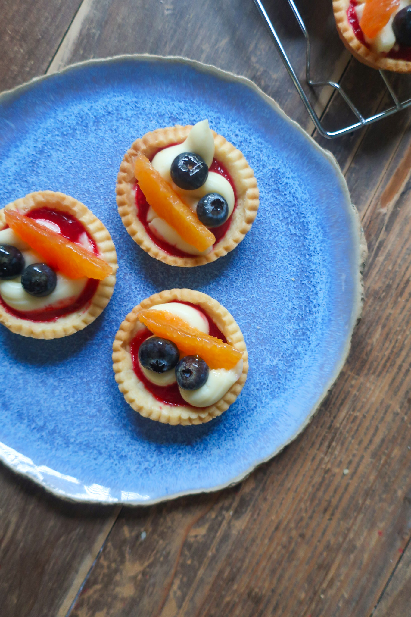 pastry crust for mini fruit tarts with pastry cream, raspberry sauce, and fresh fruit (blueberries and orange); mini pie crust on wire rack