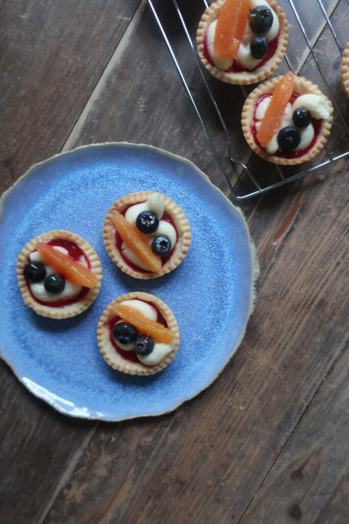 pastry crust for mini fruit tarts with pastry cream, raspberry sauce, and fresh fruit (blueberries and orange); mini pie crust on wire rack