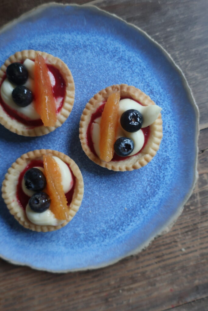 pastry crust for mini fruit tarts with pastry cream, raspberry sauce, and fresh fruit (blueberries and orange); mini pie crust on wire rack