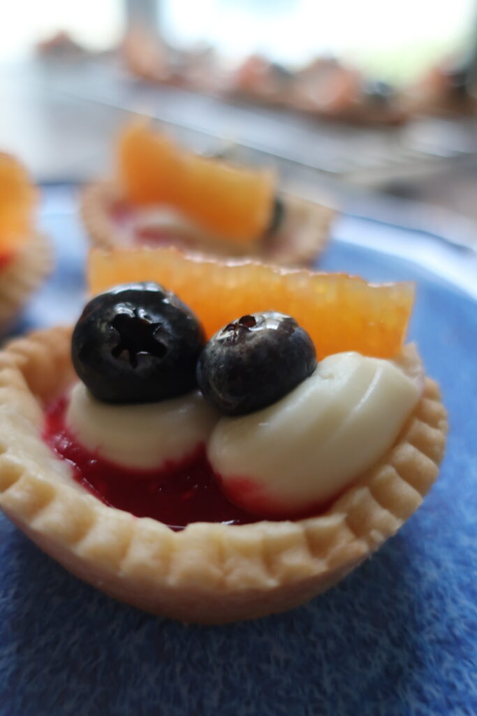 pastry crust for mini fruit tarts with pastry cream, raspberry sauce, and fresh fruit (blueberries and orange); mini pie crust on wire rack