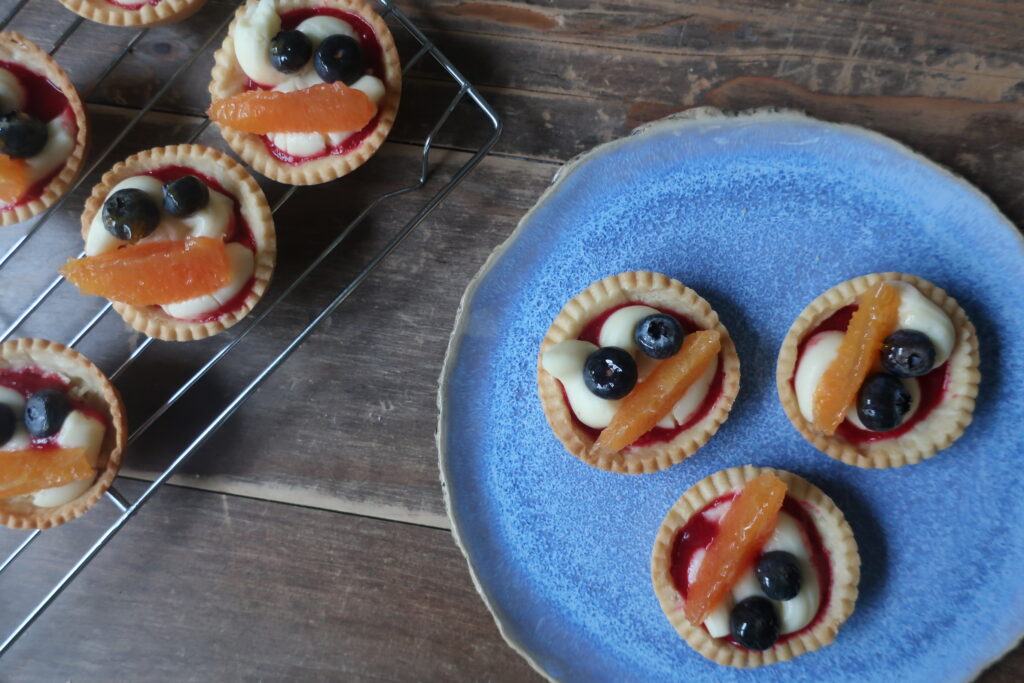 pastry crust for mini fruit tarts with pastry cream, raspberry sauce, and fresh fruit (blueberries and orange); mini pie crust on wire rack