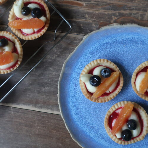 pastry crust for mini fruit tarts with pastry cream, raspberry sauce, and fresh fruit (blueberries and orange); mini pie crust on wire rack