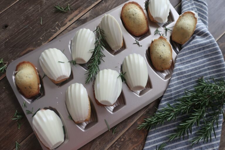 rosemary madeleines with a white chocolate shell in madeleine pan surrounded by fresh rosemary and striped blue napkin