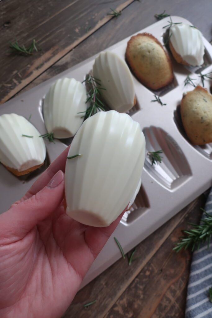 rosemary madeleines with a white chocolate shell in madeleine pan surrounded by fresh rosemary and striped blue napkin