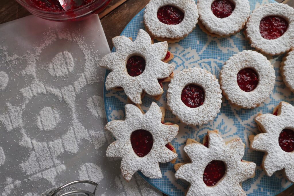 linzer cookie sandwiches with raspberry jam in the middle and dusted with powdered sugar on top; star and circle shaped linzer cookies on flowery blue plate