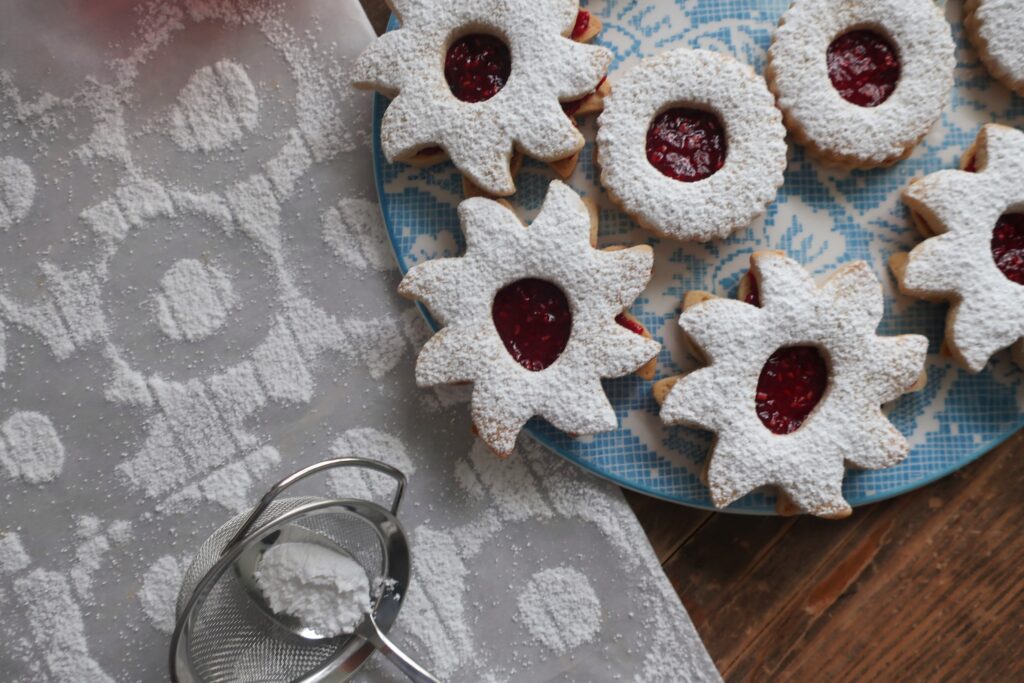 linzer cookie sandwiches with raspberry jam in the middle and dusted with powdered sugar on top; star and circle shaped linzer cookies on flowery blue plate