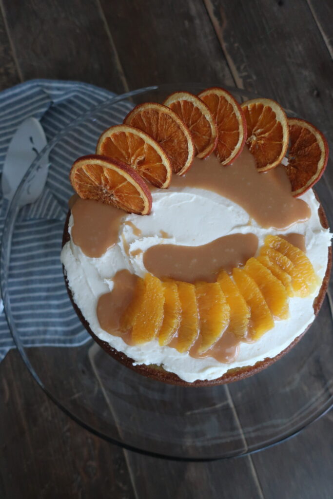 orange olive oil cake topped with brown butter cream cheese frosting, homemade caramel sauce, and dehydrated oranges