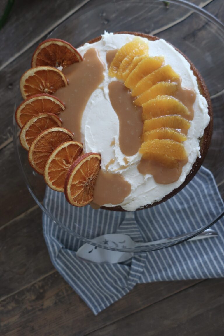 orange olive oil cake topped with brown butter cream cheese frosting, homemade caramel sauce, and dehydrated oranges