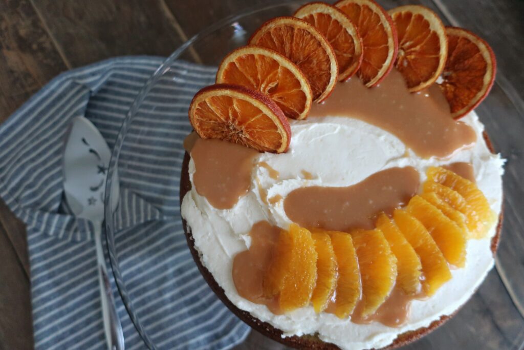 orange olive oil cake topped with brown butter cream cheese frosting, homemade caramel sauce, and dehydrated oranges