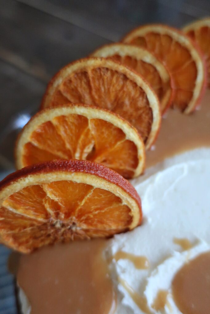 orange olive oil cake topped with brown butter cream cheese frosting, homemade caramel sauce, and dehydrated oranges