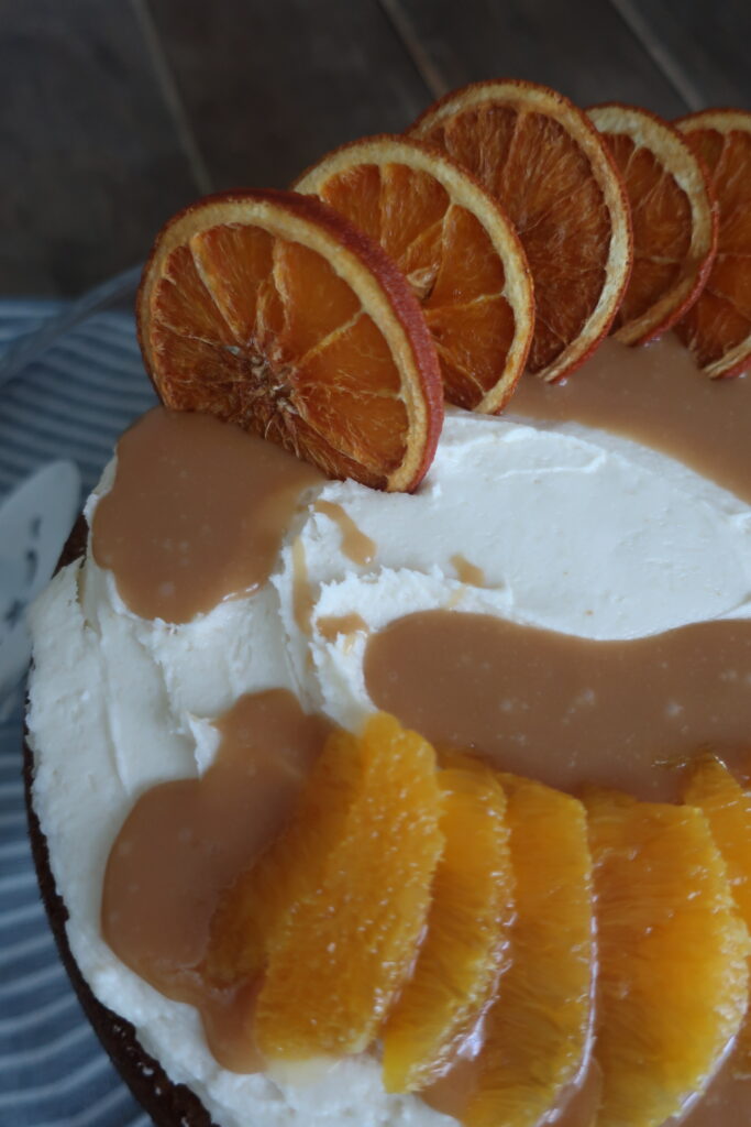 orange olive oil cake topped with brown butter cream cheese frosting, homemade caramel sauce, and dehydrated oranges