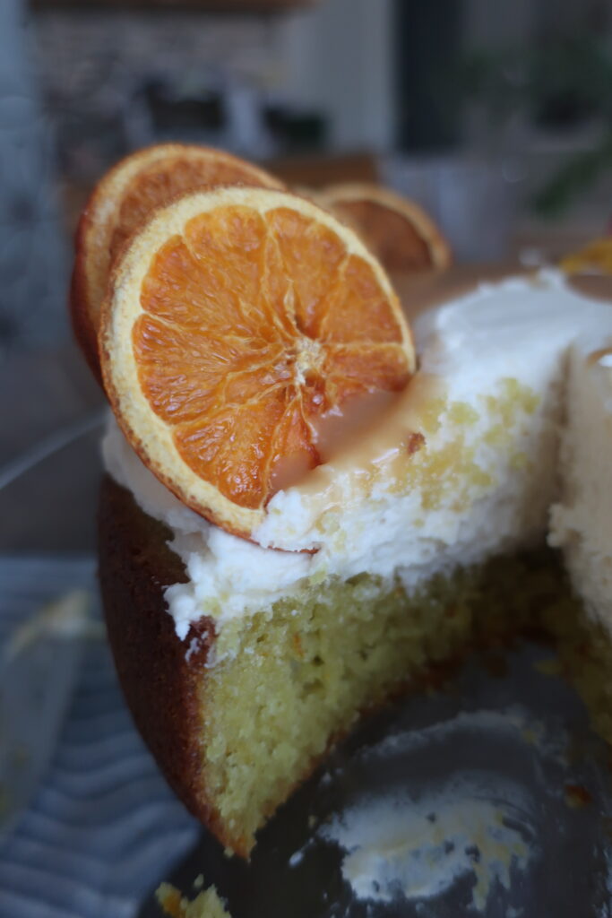 inside look at orange olive oil cake topped with brown butter cream cheese frosting, homemade caramel sauce, and dehydrated oranges