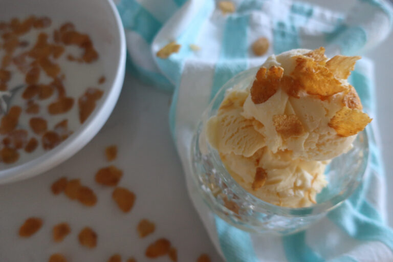 dish of cereal milk ice cream topped with cornflakes; blue and white striped towel with bowl of cornflakes in bowl with milk