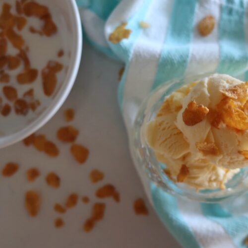 dish of cereal milk ice cream topped with cornflakes; blue and white striped towel with bowl of cornflakes in bowl with milk