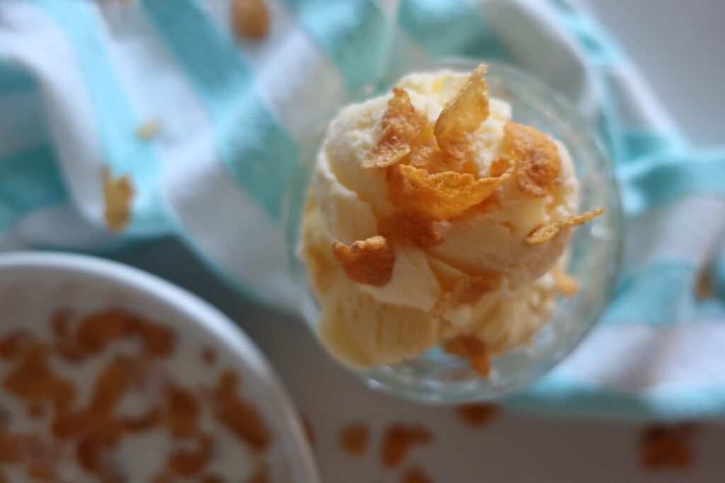 dish of cereal milk ice cream topped with cornflakes; blue and white striped towel with bowl of cornflakes in bowl with milk