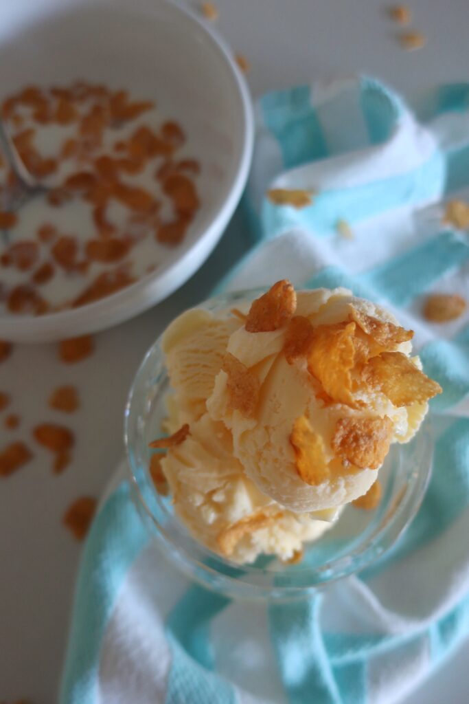 dish of cereal milk ice cream topped with cornflakes; blue and white striped towel with bowl of cornflakes in bowl with milk