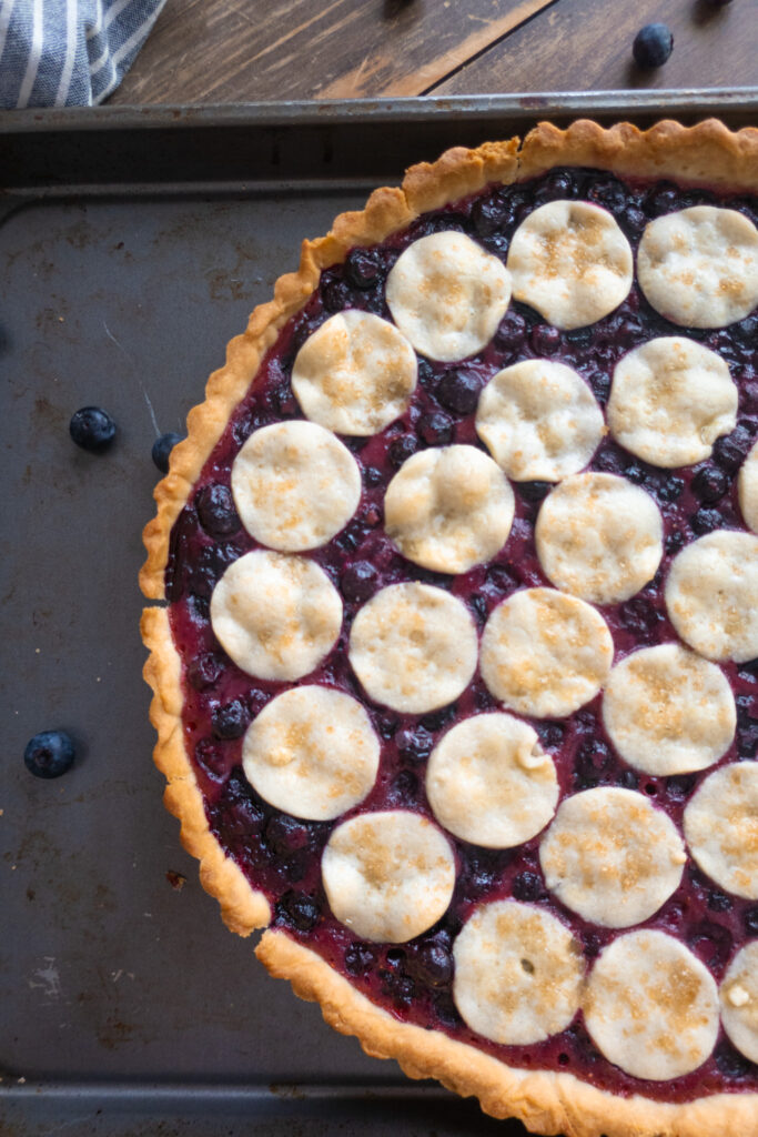 blueberry tart in baking sheet next to blue striped napkin