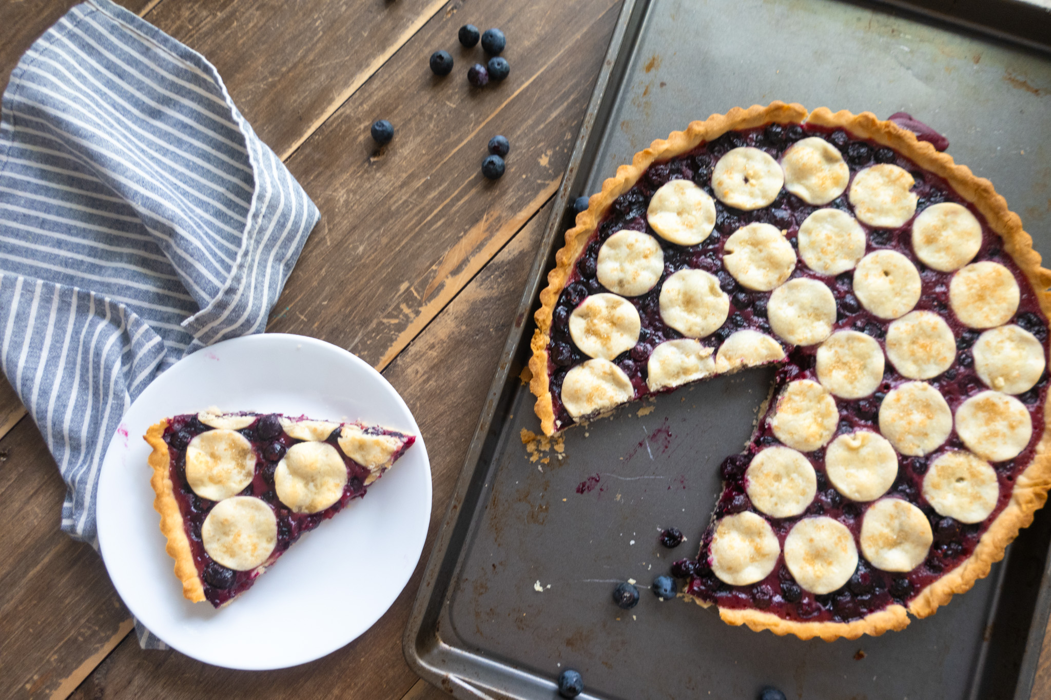 slice of blueberry tart in baking sheet next to blue striped napkin