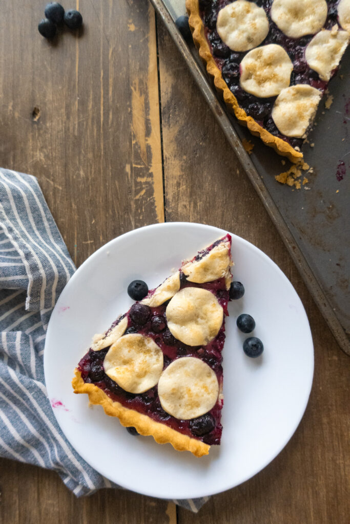 slice of blueberry tart in baking sheet next to blue striped napkin