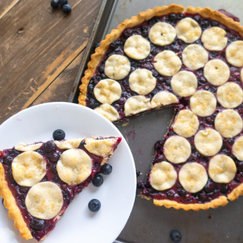 slice of blueberry tart in baking sheet next to blue striped napkin