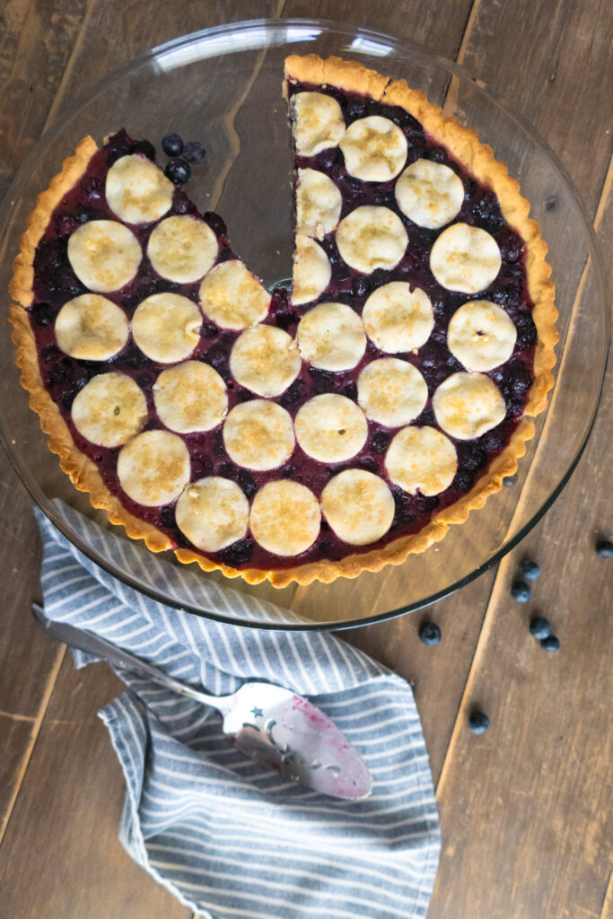 blueberry tart on glass cake tray next to blue striped napkin