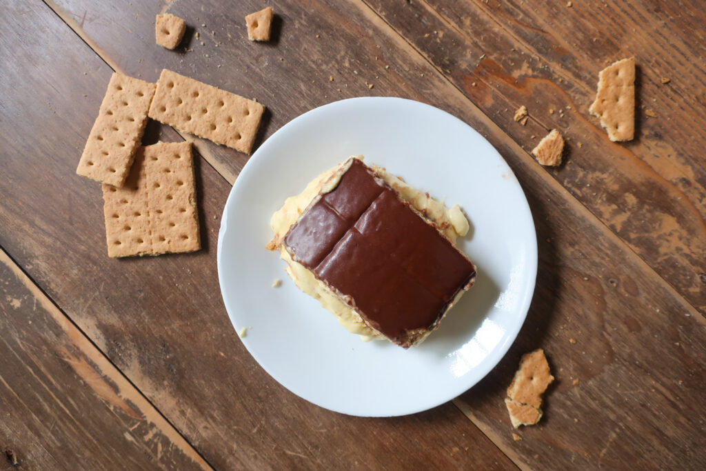 no bake chocolate eclair cake with french vanilla cream layered with graham crackers and topped with chocolate