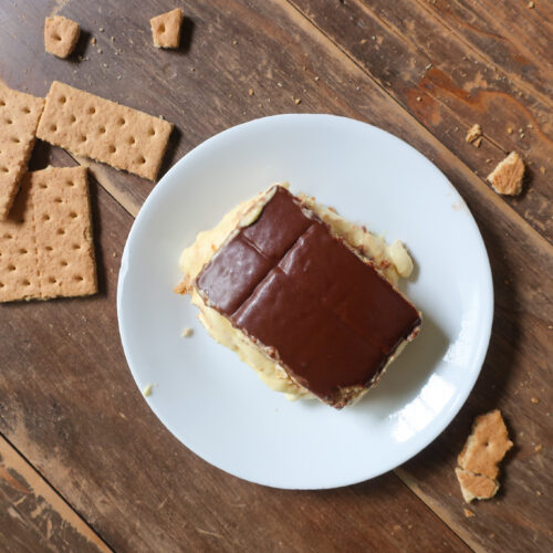 no bake chocolate eclair cake with french vanilla cream layered with graham crackers and topped with chocolate