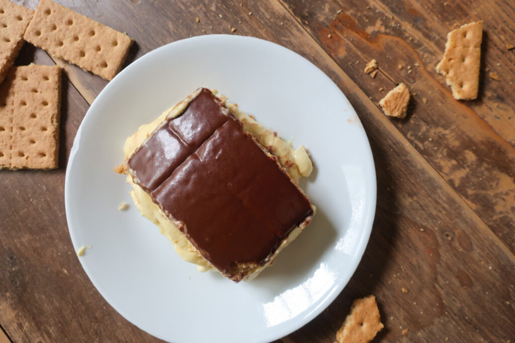 no bake chocolate eclair cake with french vanilla cream layered with graham crackers and topped with chocolate