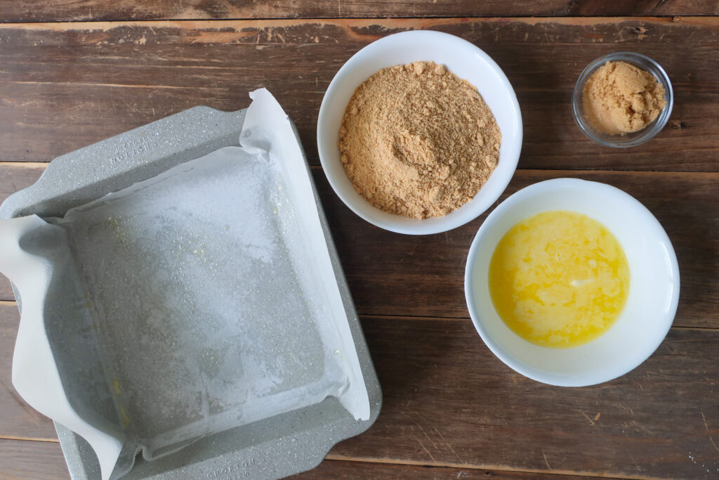 makings of a graham cracker crust; butter and graham crackers next to 9x9 pan for graham cracker crust for key lime cheesecake bars with graham cracker crust and topped with fresh whipped cream