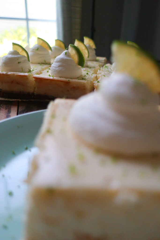 key lime cheesecake bars with graham cracker crust and topped with fresh whipped cream