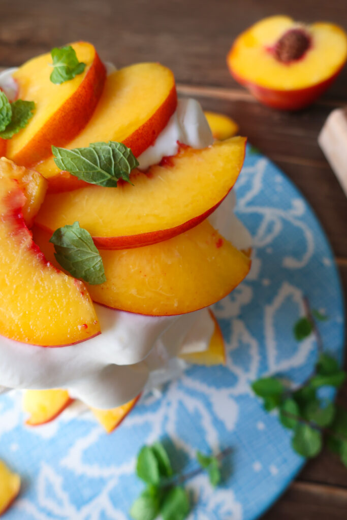 minty peach pavlova; two tiers of french meringue stacked with whipped cream, slices of fresh peaches, and chopped fresh mint