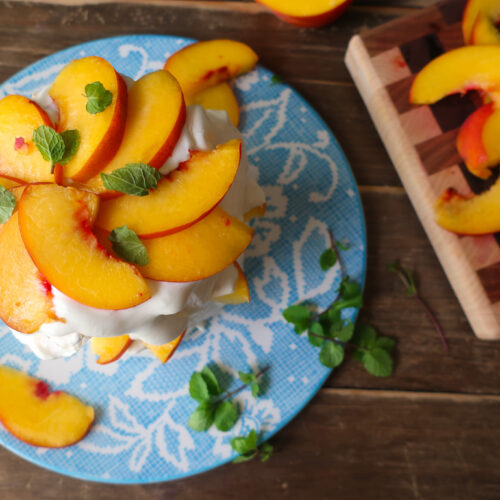 minty peach pavlova; two tiers of french meringue stacked with whipped cream, slices of fresh peaches, and chopped fresh mint