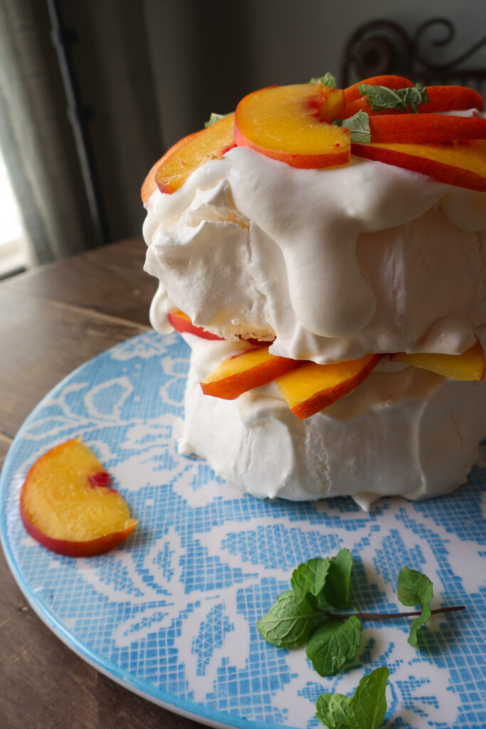 minty peach pavlova; two tiers of french meringue stacked with whipped cream, slices of fresh peaches, and chopped fresh mint