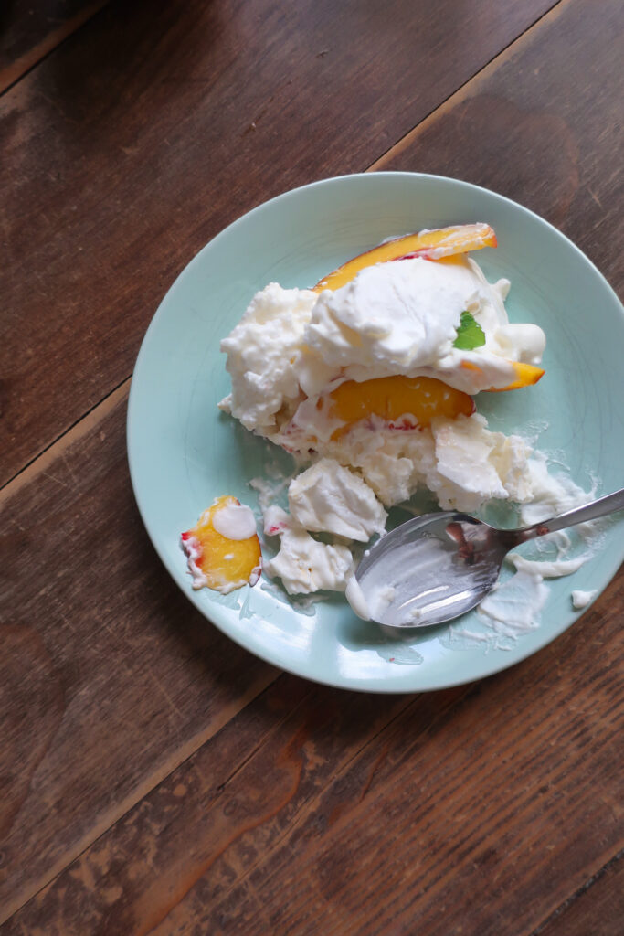 partially eaten piece of minty peach pavlova; two tiers of french meringue stacked with whipped cream, slices of fresh peaches, and chopped fresh mint