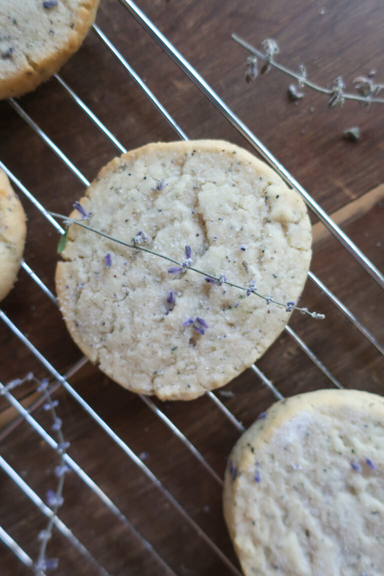 upclose of earl grey and lavender shortbread cookies on wire rack next to pitcher of fresh lavender and metal spatula