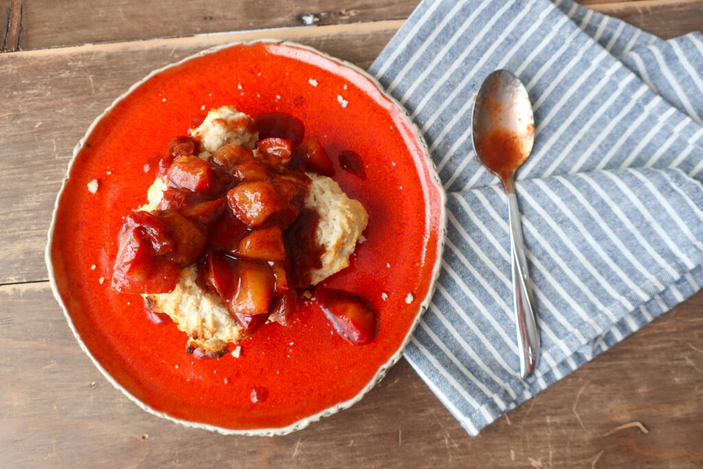 single serve drop biscuit with cinnamon plum compote sitting on orange plate with blue striped napkin and spoon