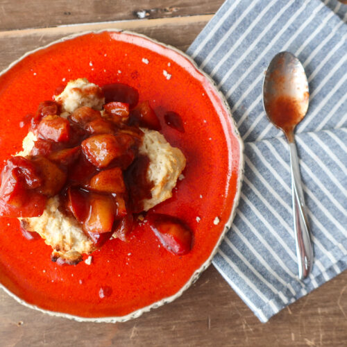 single serve drop biscuit with cinnamon plum compote sitting on orange plate with blue striped napkin and spoon