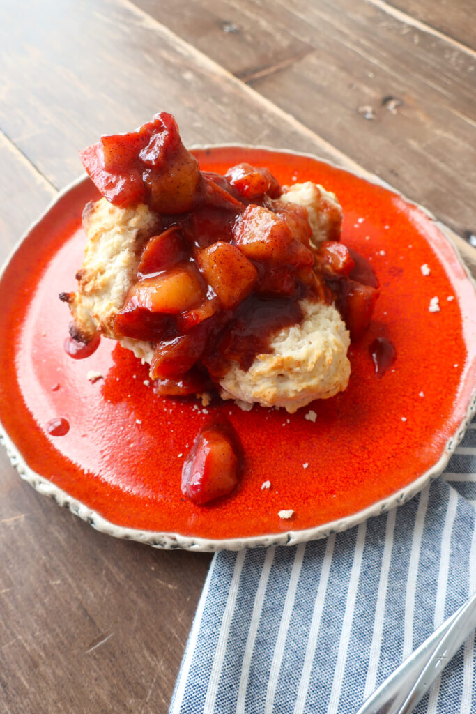 single serve drop biscuit with cinnamon plum compote sitting on orange plate with blue striped napkin and spoon