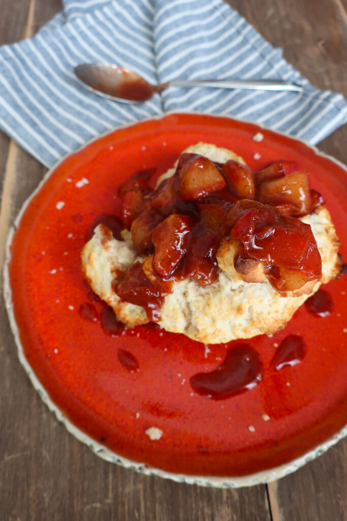 single serve drop biscuit with cinnamon plum compote sitting on orange plate with blue striped napkin and spoon