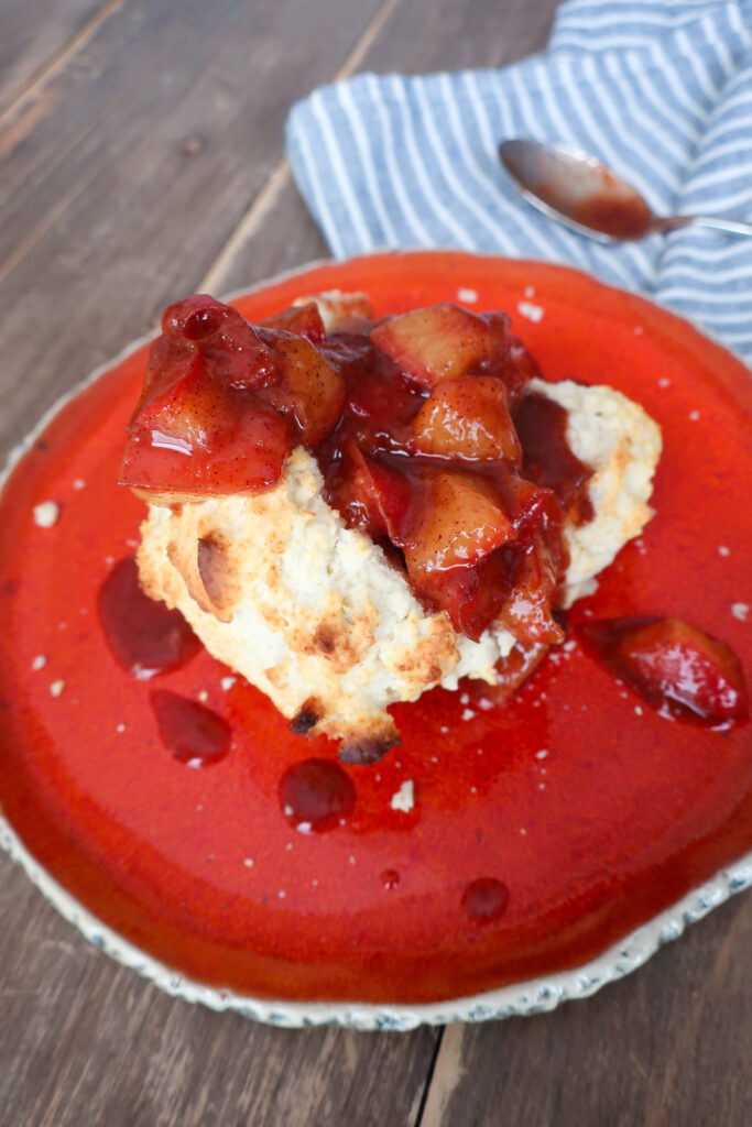 single serve drop biscuit with cinnamon plum compote sitting on orange plate with blue striped napkin and spoon