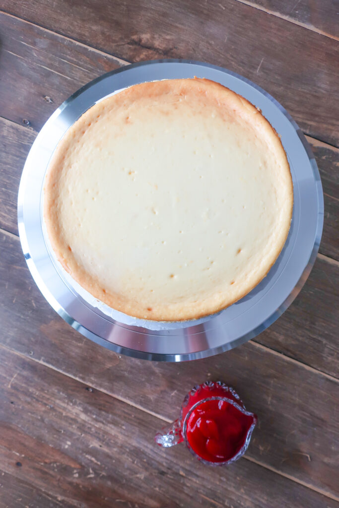 undecorated orange cheesecake with cranberry sauce in pitcher on the side; orange cheesecake with cinnamon spiced graham cracker crust and topped with cranberry sauce